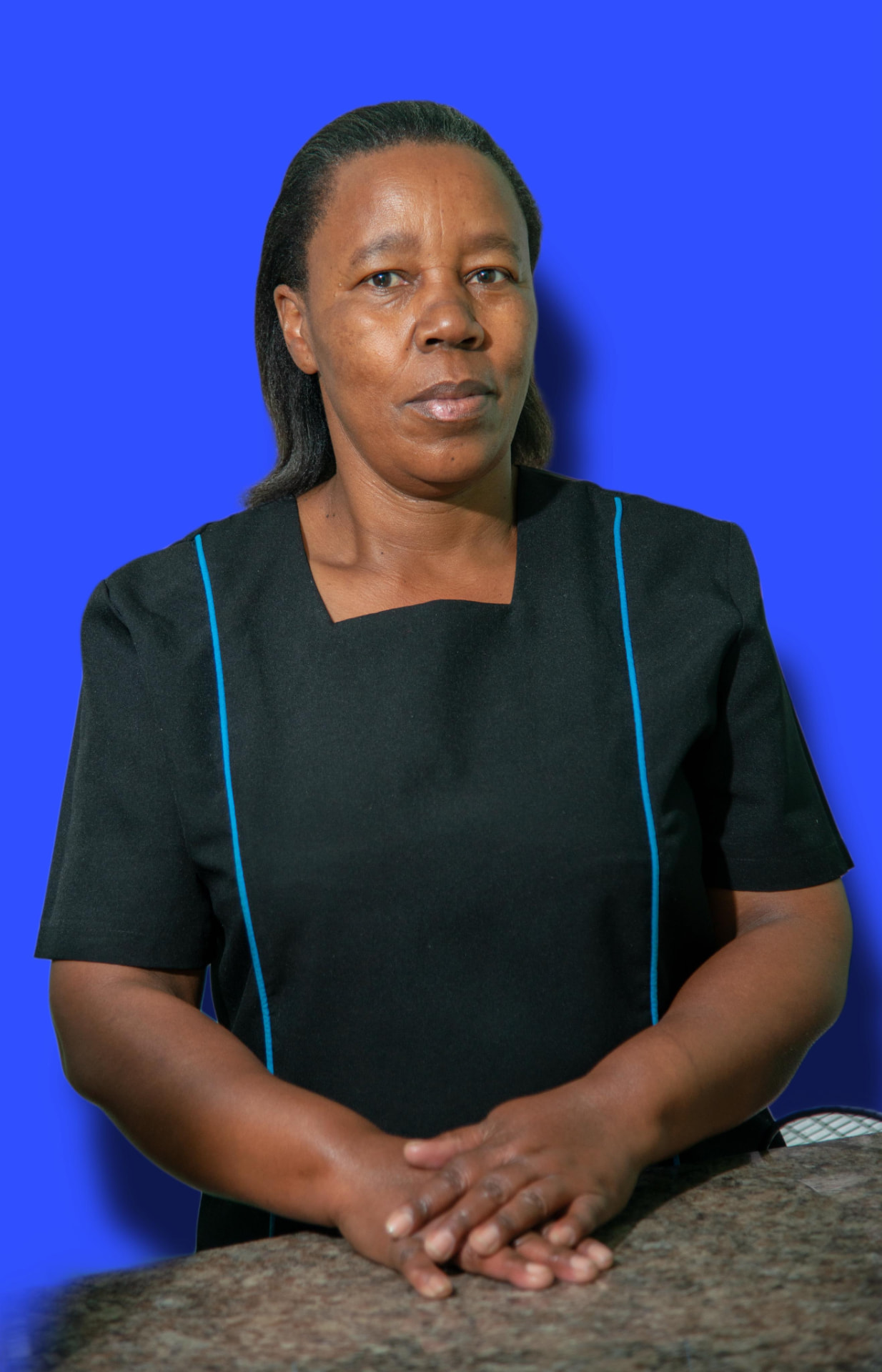 Rebecca Molatedi, the cleaner at Dr T Matseke Practice, standing at her workstation in a black uniform with blue piping against a blue background